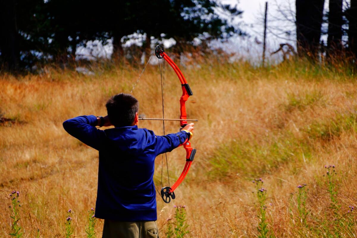 Criança com arco e flecha em um campo gramado.