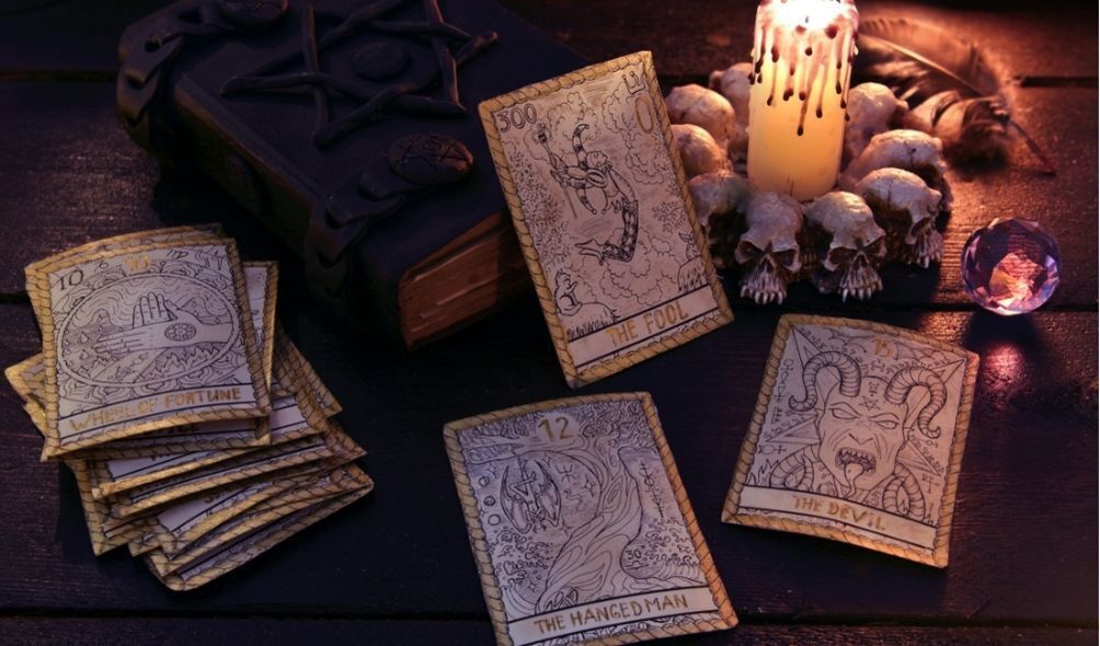 Cartas de tarô "O Louco", "O Enforcado" e "O Diabo" ao lado de uma vela