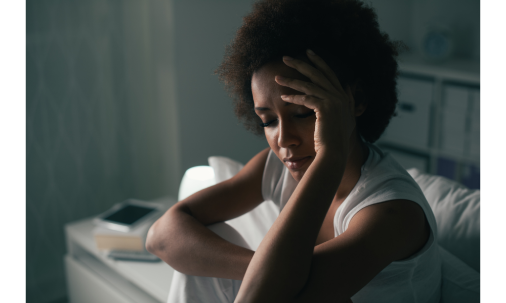 Mulher sentada na cama com expressão de angústia e mão sobre a cabeça.