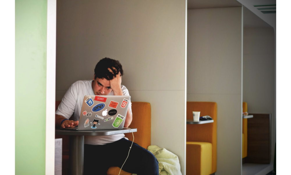 Homem preocupado com o trabalho sentado com um notebook e mão sobre a cabeça.