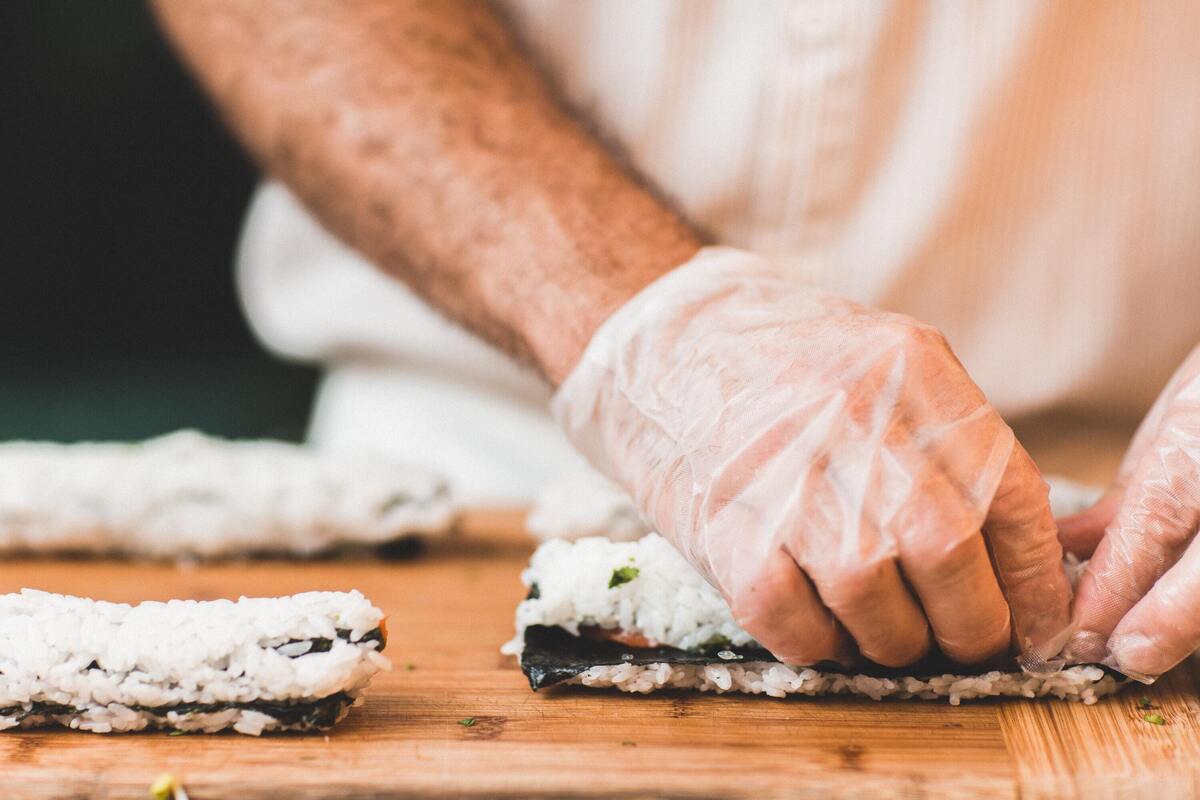 Mãos de um homem enrolando sushi.