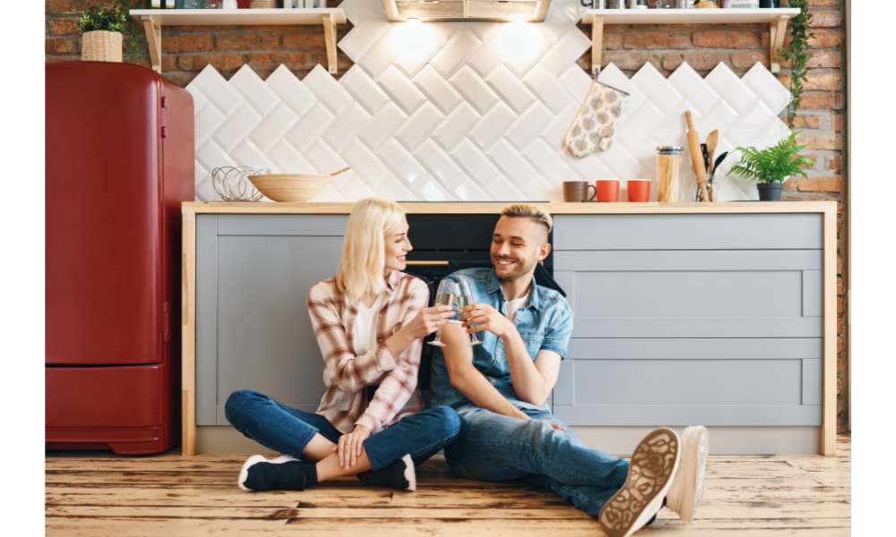 Casal sentado no chão de uma cozinha tomando champagne.