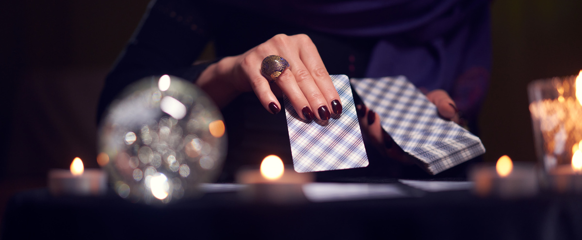 Imagem da mão de uma mulher, com as unhas pintadas de vinho, fazendo uma tiragem de tarot