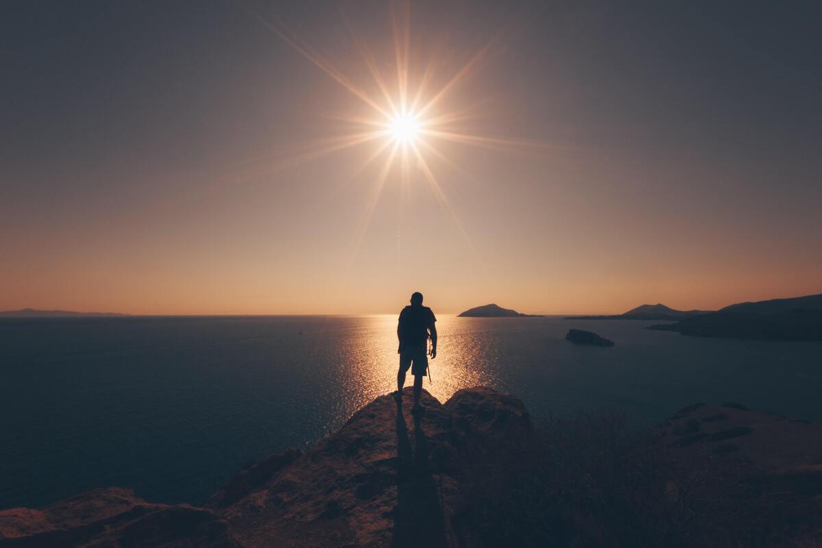 Silhueta de um homem em uma pedra, sol ao fundo.