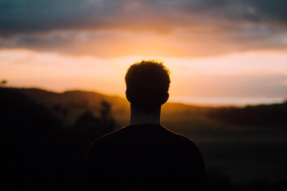 Homem de costas, pôr do sol ao fundo. 