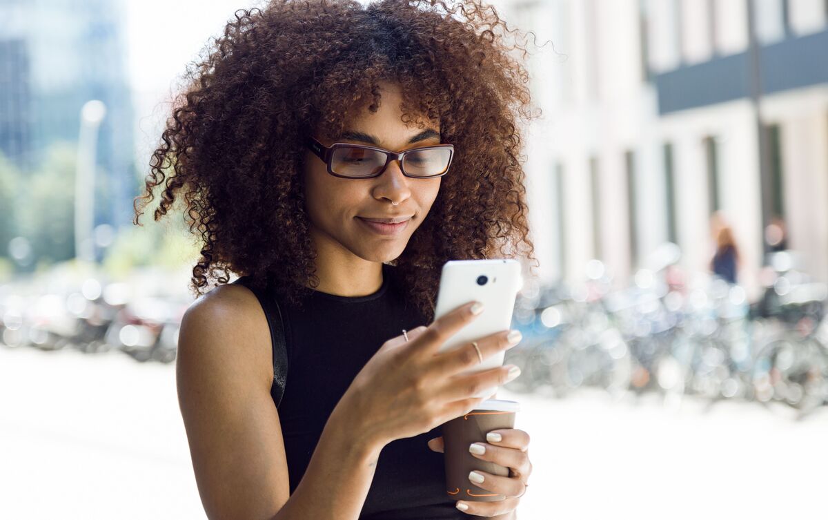 Mulher usando celular branco na rua.