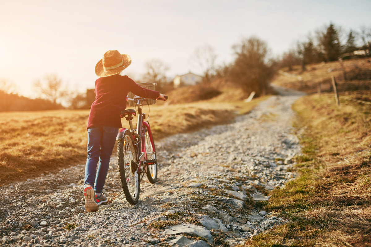 Uma mulher empurrando uma bicicleta em uma estrada de terra