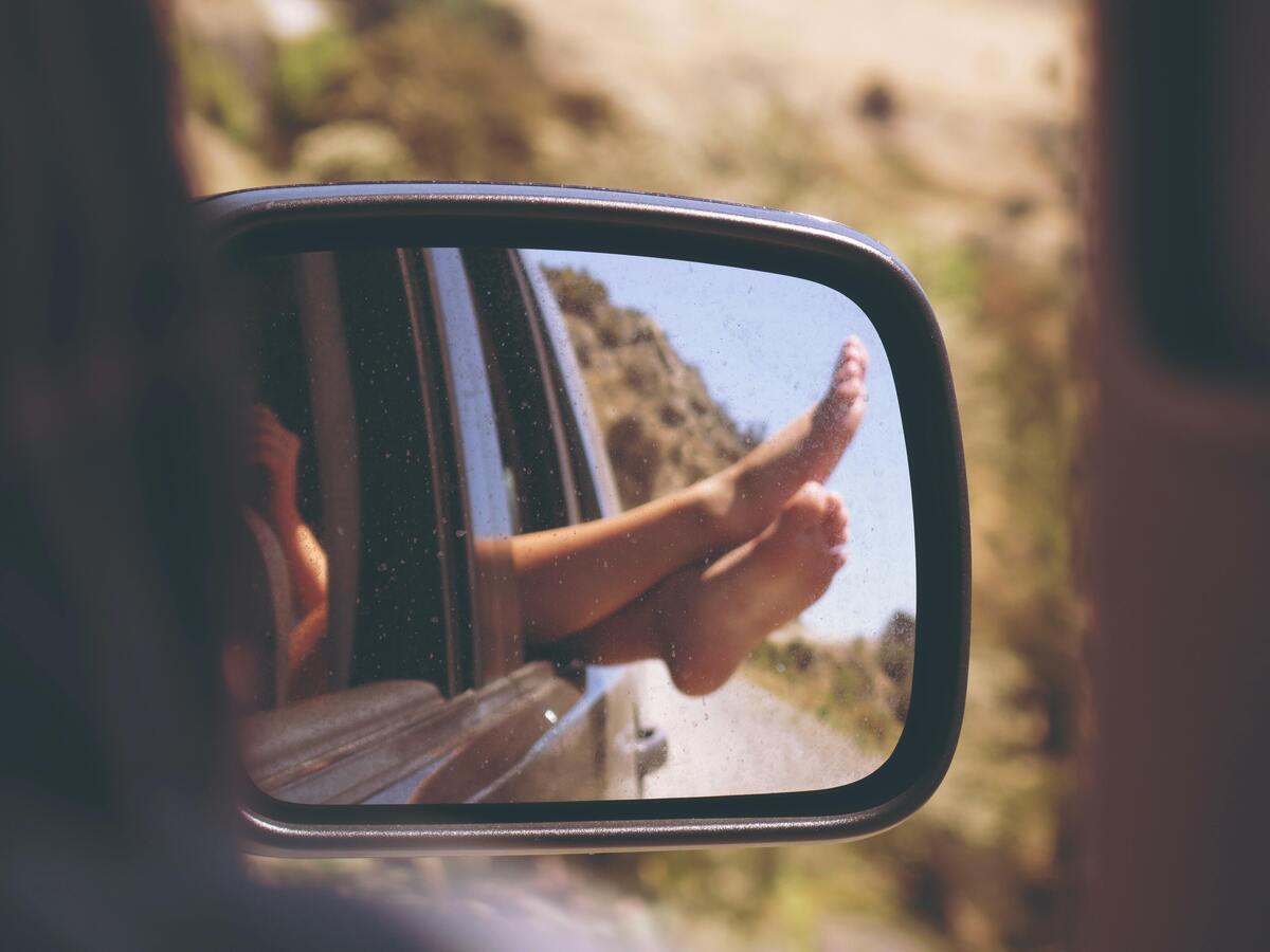 Mulher com os pés para fora da janela na estrada, visão do retrovisor. 