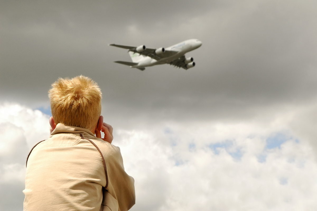 Criança vendo avião no céu, enquanto tampa os ouvidos.