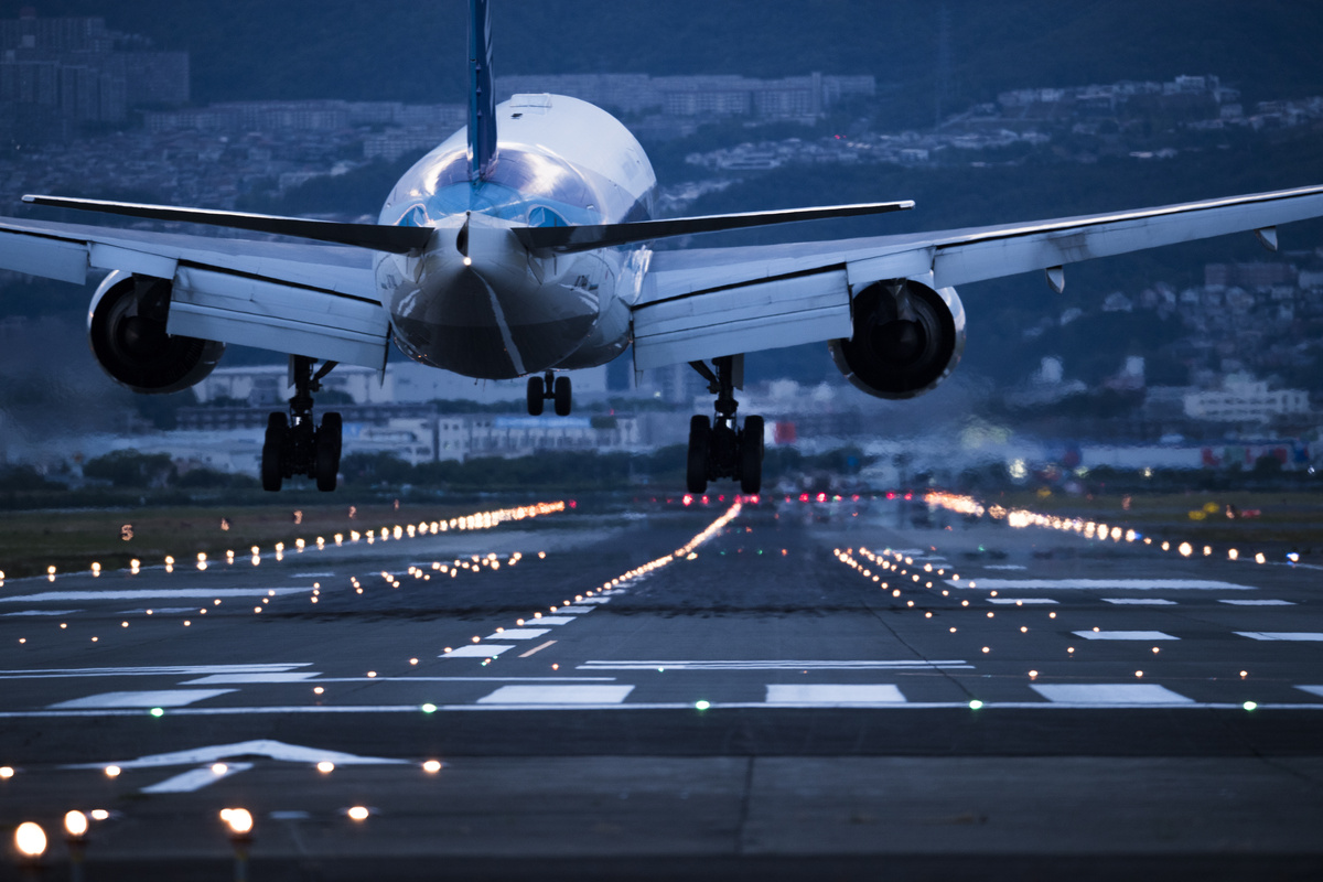 Avião decolando em pista iluminada durante o entardecer. 