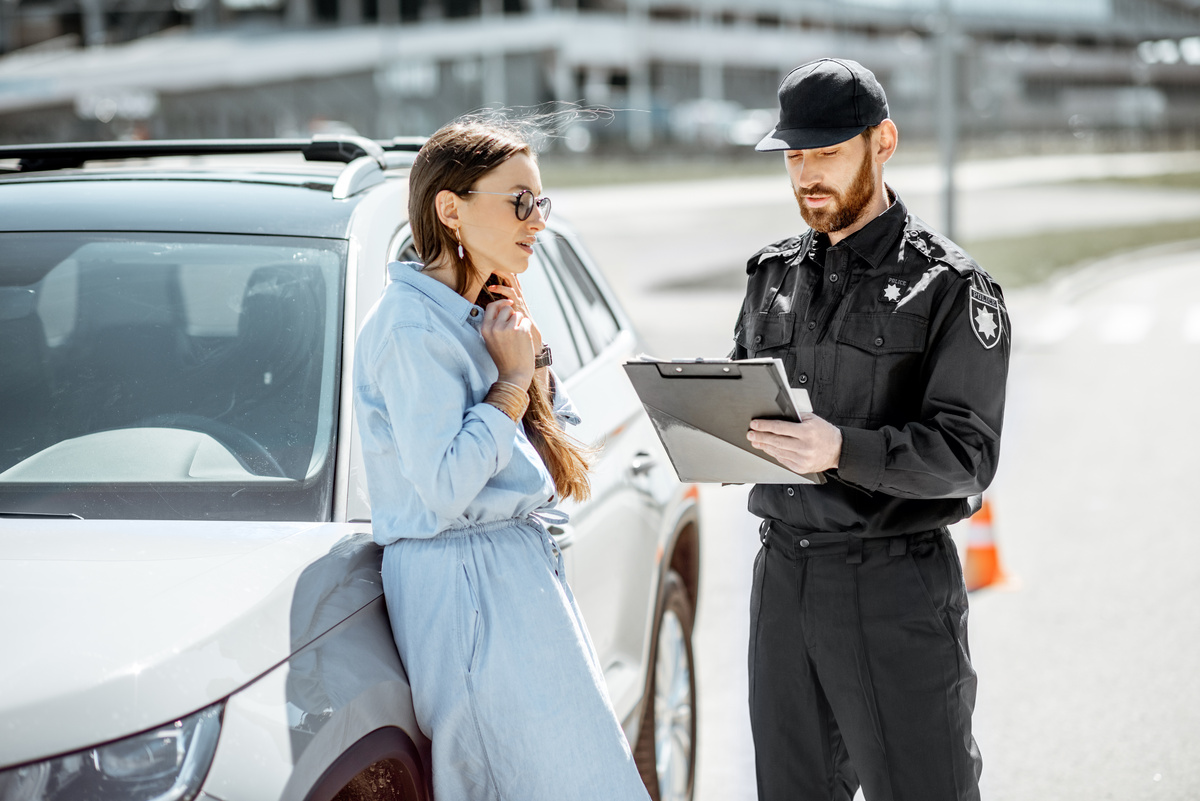 Uma mulher encostada em um carro e um homem escrevendo em uma prancheta