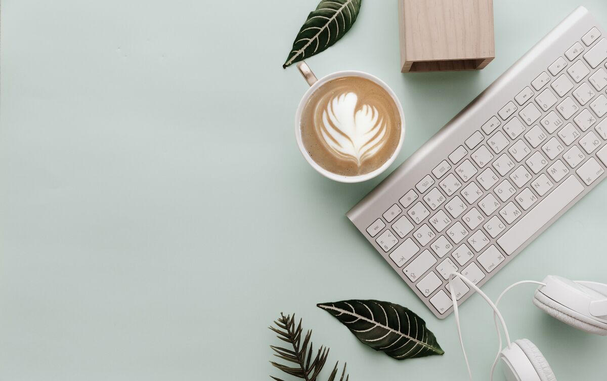 Mesa com teclado de computador e caneca com café.