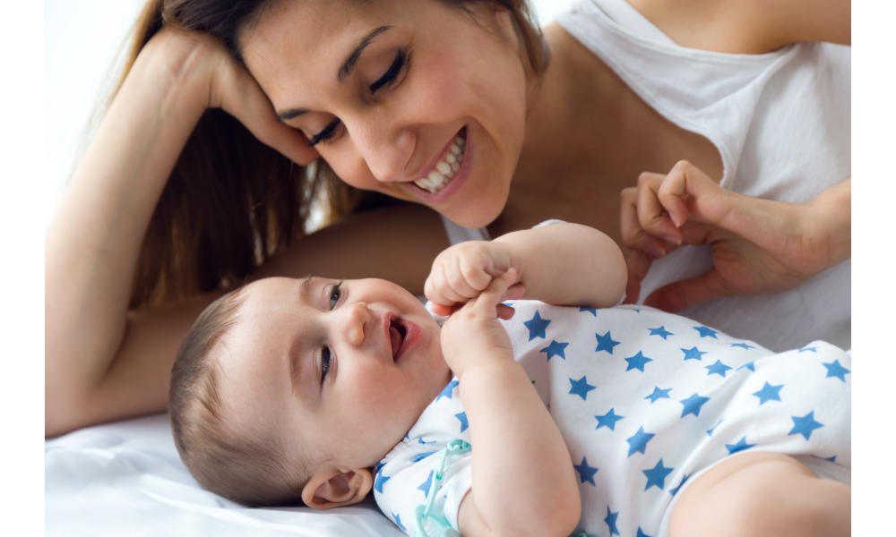 Mãe brincando seu bebê na cama.