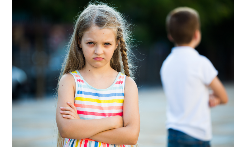 Menina chateada de braços cruzados, atrás um menino de costas.