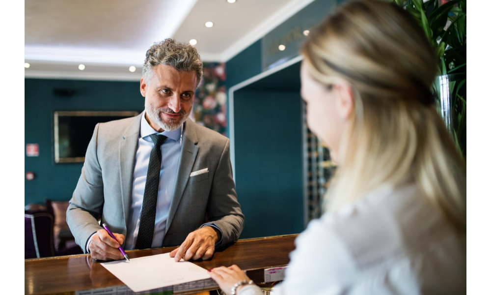 Homem na recepção de um hotel, falando com a recepcionista.