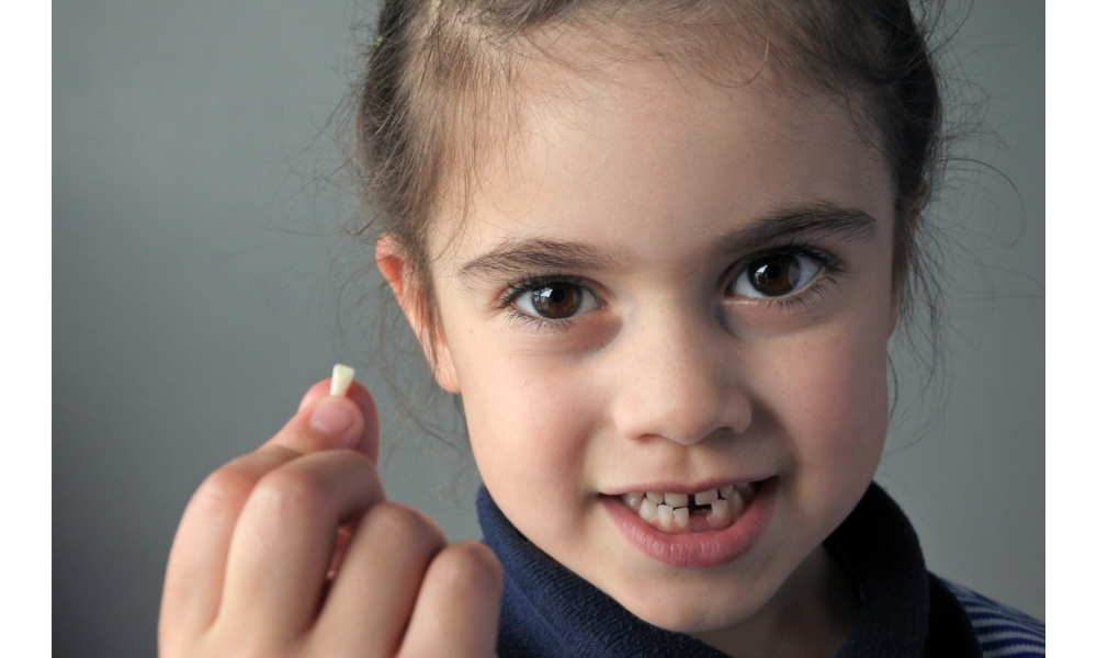 Menina segurando um dente seu que caiu.