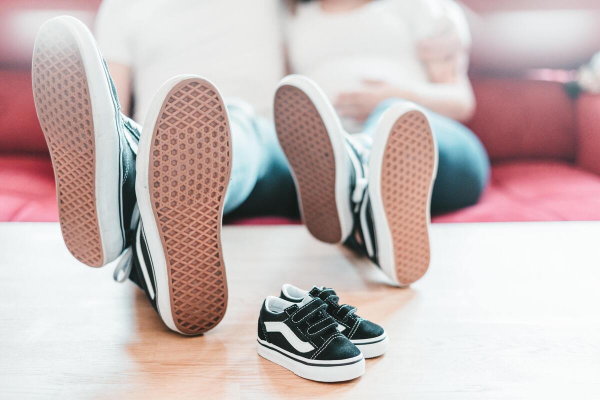 Casal de tênis com os pés apoiados na mesa e um tênis infantil na mesa. 